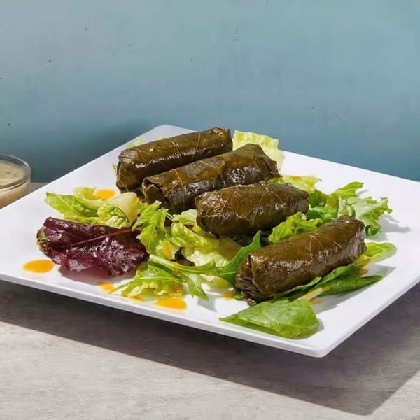 Four dolmades, or stuffed grape leaves, on a bed of mixed greens with a light dressing.
