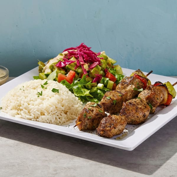 Grilled chicken and vegetable skewers with rice and a fresh salad on a white rectangular plate.