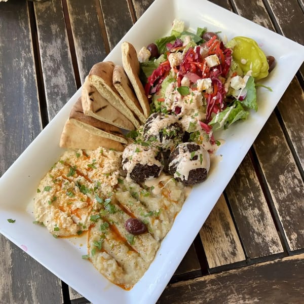 A white platter with falafel, hummus, baba ghanoush, pita bread, and a fresh salad.