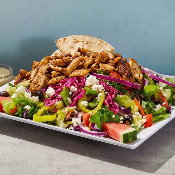 A large salad with grilled chicken, feta, olives, red cabbage, and watermelon, served with pita.
