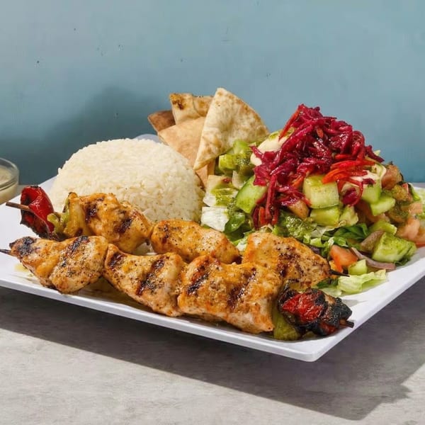 Grilled chicken skewers with rice, pita bread, and a fresh salad topped with red cabbage.